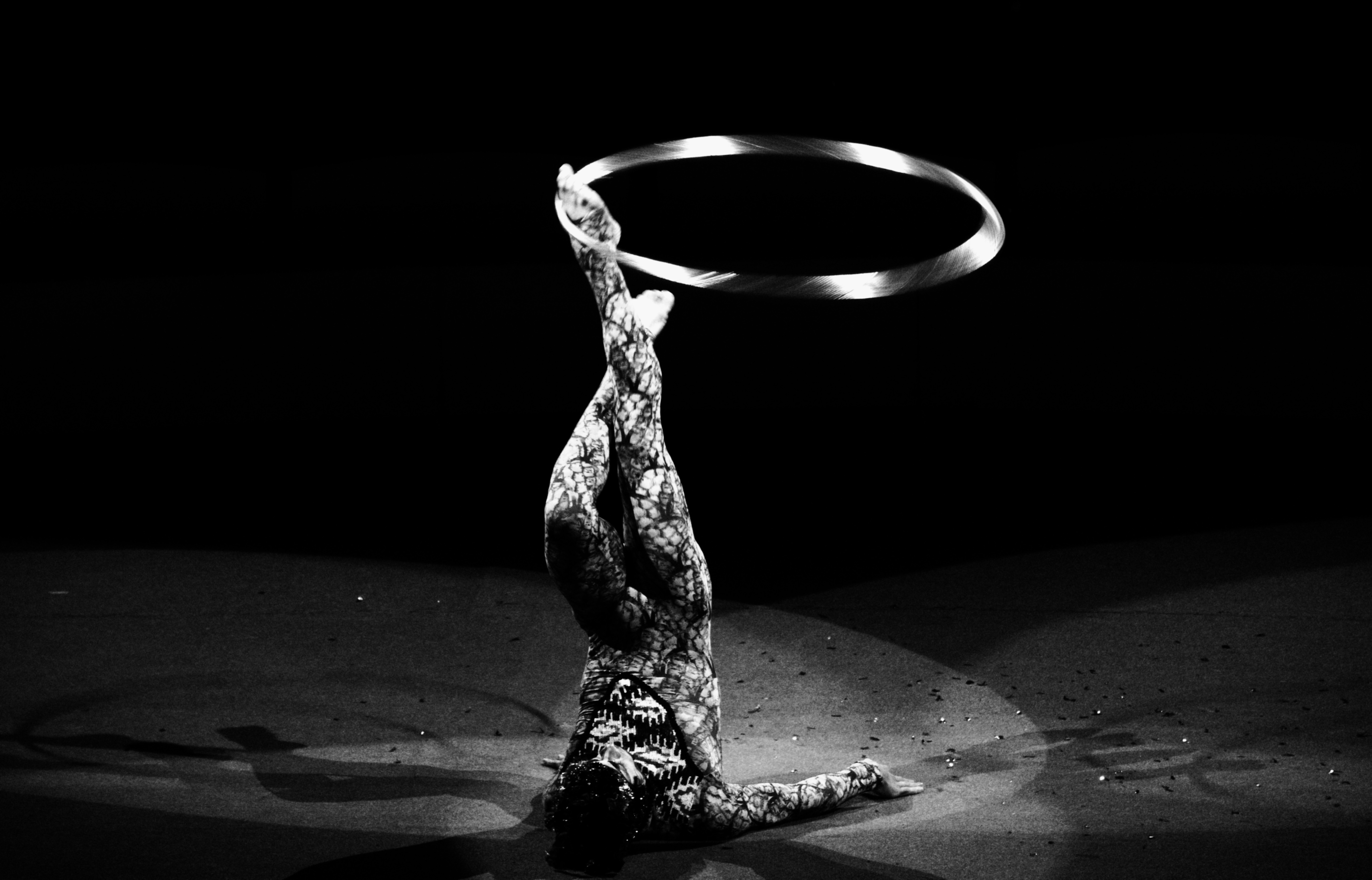 Acrobat lying on floor spinning a luminous hoop with feet raised